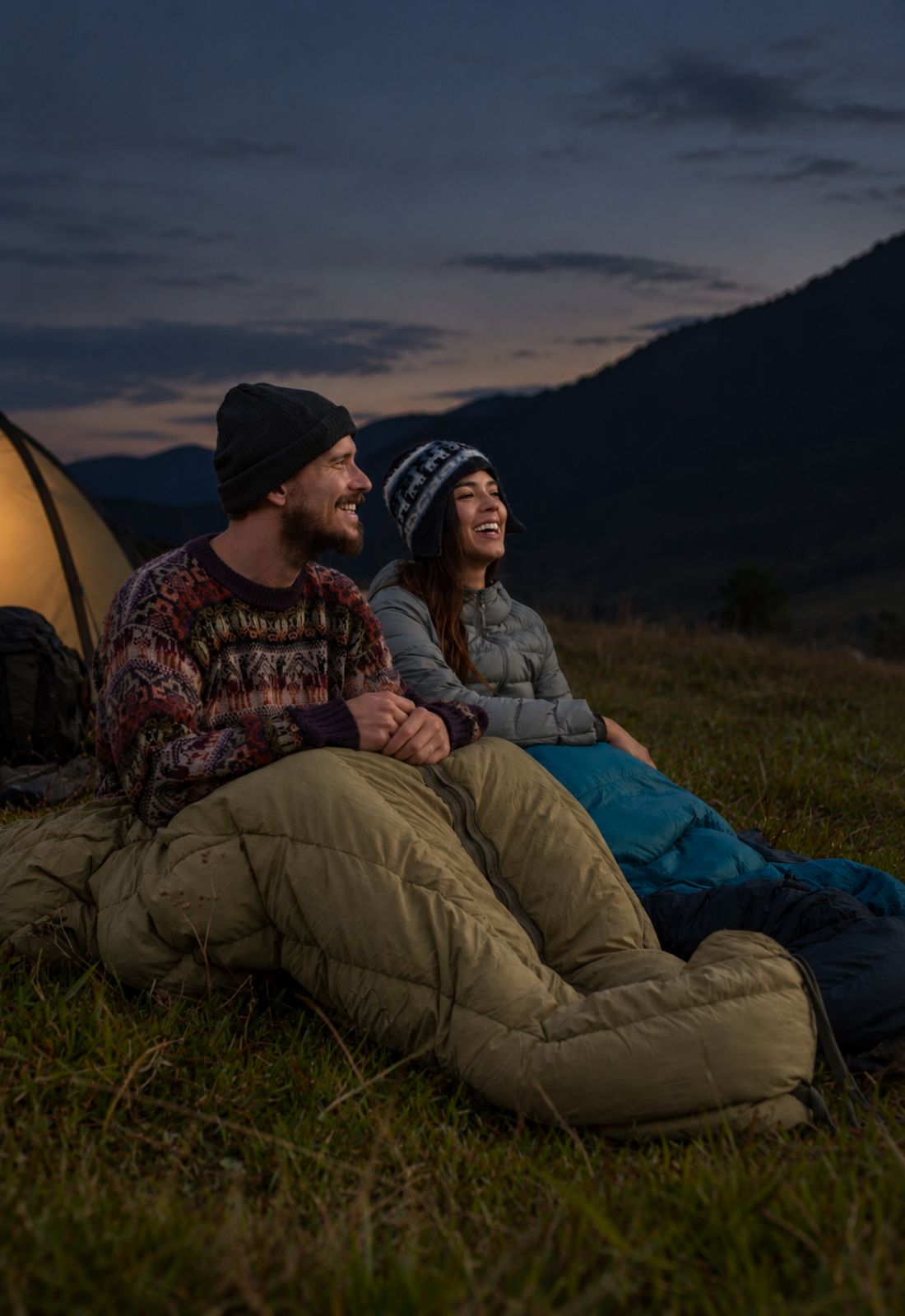 Couple laughs together in sleeping bags during a mountain campsite evening